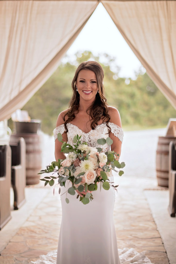 Bride walking down the aisle, holding a bouquet of white flowers, stops to smile for the camera